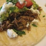 Slow Cooker Mexican Pulled Pork on a taco with queso fresco, cilantro, and guacamole