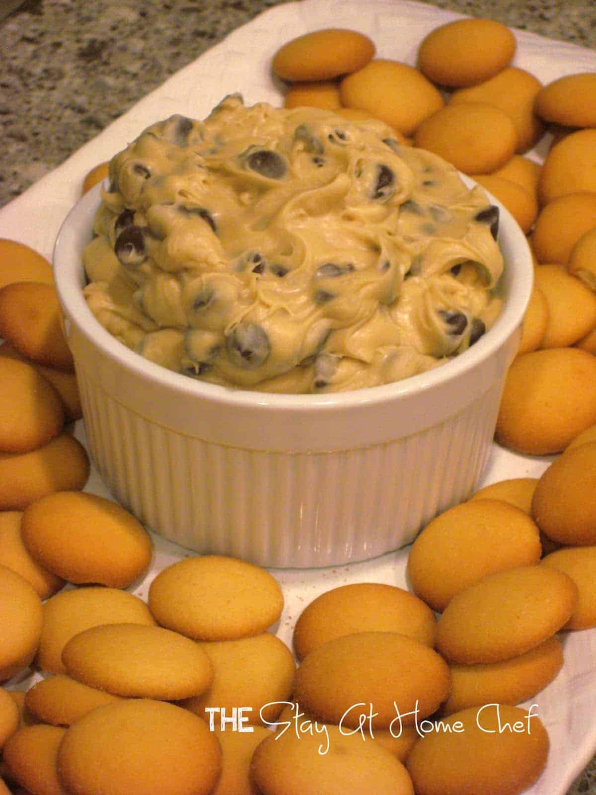 Cookie dough dip in a white glass container surrounded by cookies.