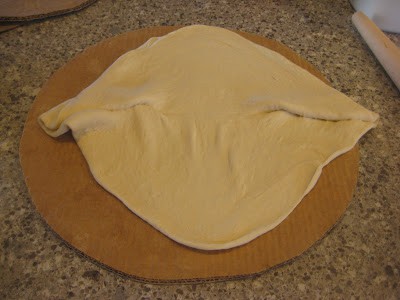 Pizza dough unfolded on cardboard cutout, a little squished but still workable.