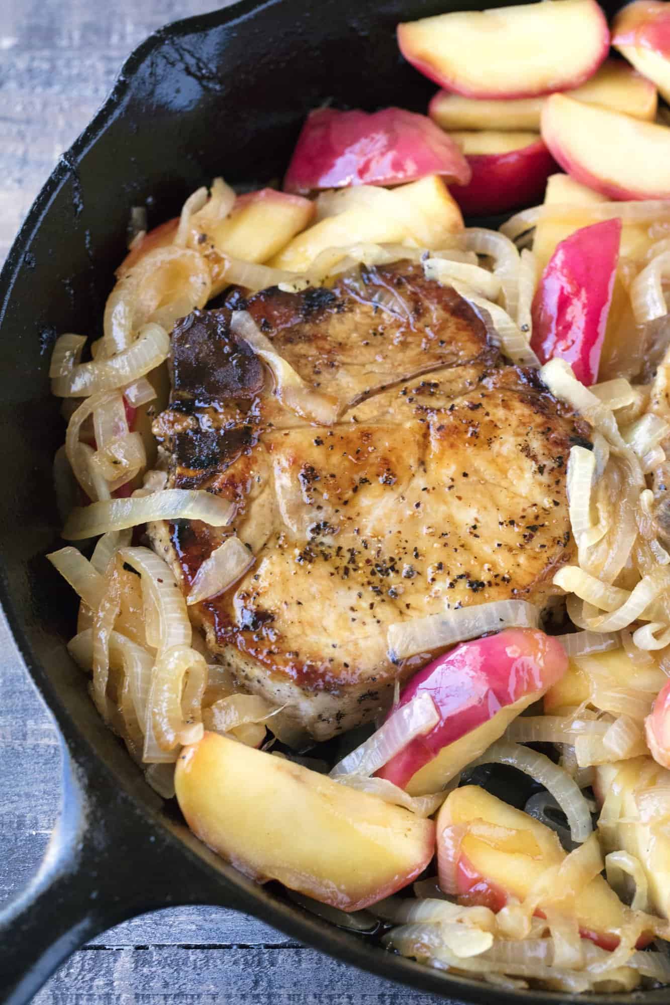 An Apple Pork Chop in a skillet with caramelized onions and apple slices