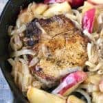 An Apple Pork Chop in a skillet with caramelized onions and apple slices