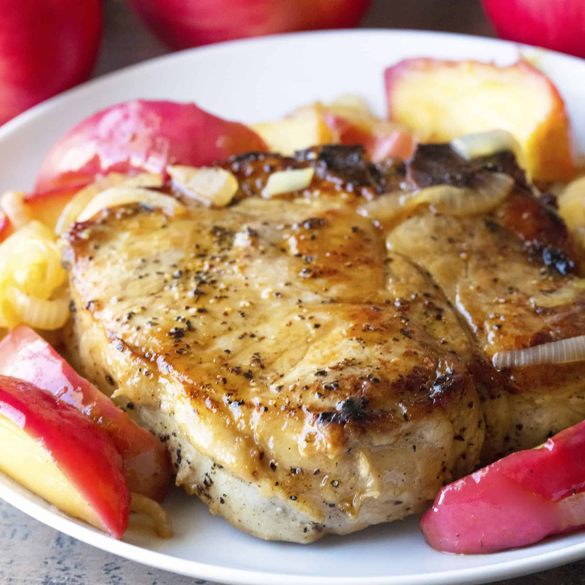 A pork chop cooked with an apple reduction, served on a plate with apple slices and caramelized onions