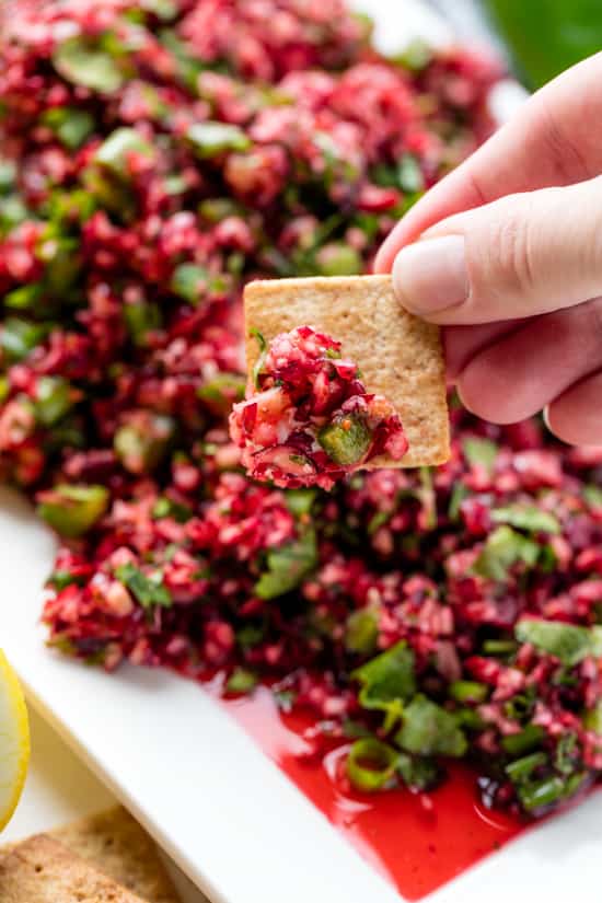 Square cracker scooping some Cranberry Salsa on a white plate.