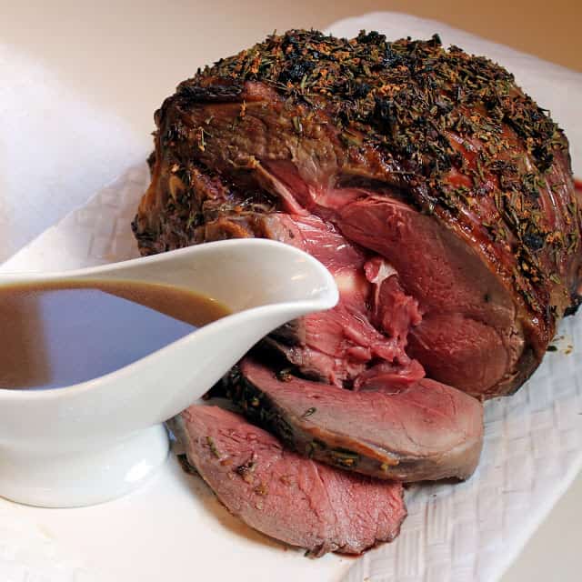 roasted leg of lamb, sliced with sauce being drizzled on top