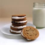 Peanutbutter chocolate marshmallow sandwiches stacked up on a white plate by a glass of milk.