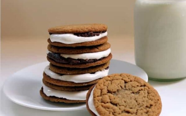 Peanutbutter chocolate marshmallow sandwiches stacked up on a white plate by a glass of milk.