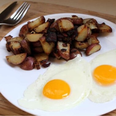 Potatoes, bacon, and eggs on a white plate.