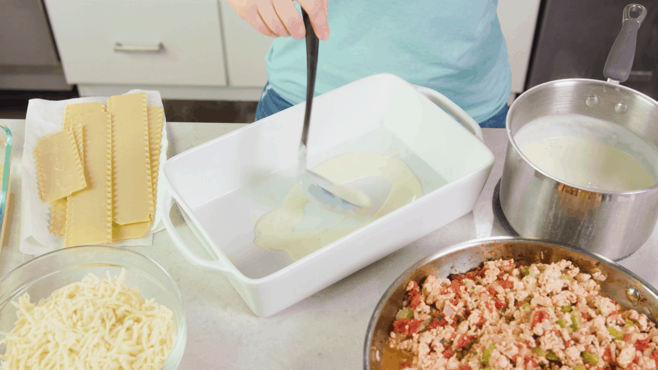 Bechamel being placed on bottom of lasagna pan.