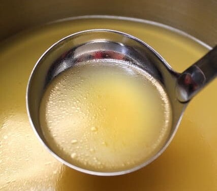 A ladle is full of chicken broth.