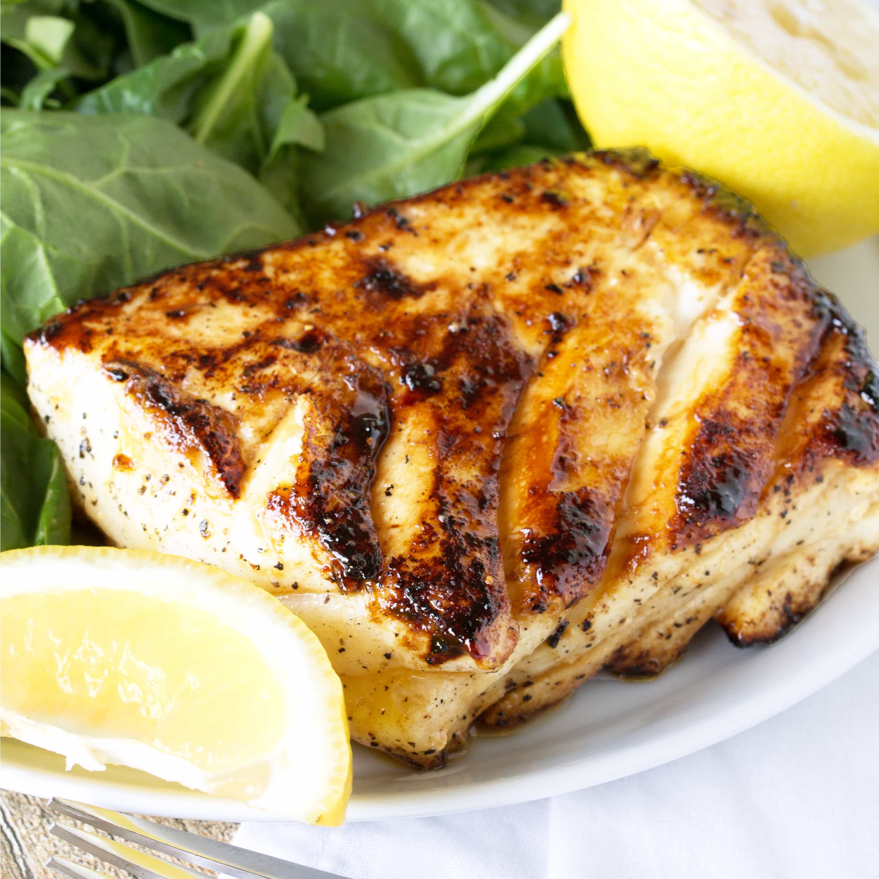 Grilled halibut with a salad and lemon wedges on a white plate with a fork nearby