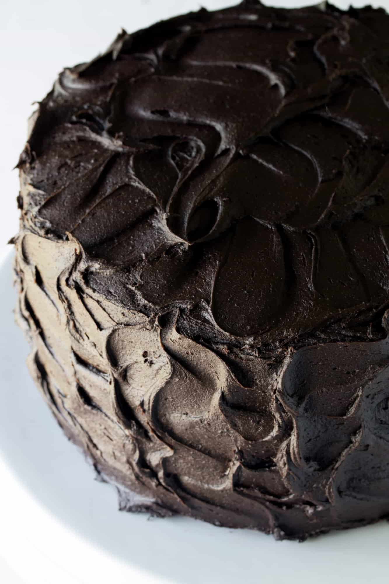 Dark and rich frosted triple layer chocolate cake with swirled chocolate frosting on a white cake stand