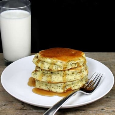 A stack of Almond Poppyseed Pancakes on a white plate with a fork and a glass of milk by it.