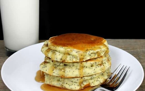 A stack of Almond Poppyseed Pancakes on a white plate with a fork and a glass of milk by it.
