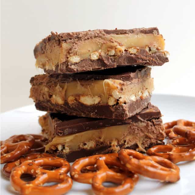 Chocolate Caramel Pretzel bars stacked on a plate, surrounded by pretzels