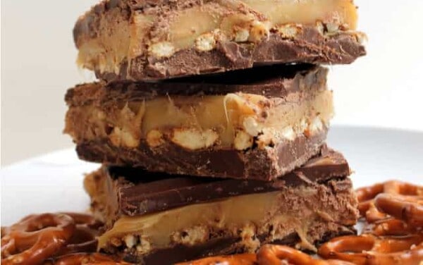 A stack of Chocolate Pretzel Caramel Bars on a white plate with pretzels around them.