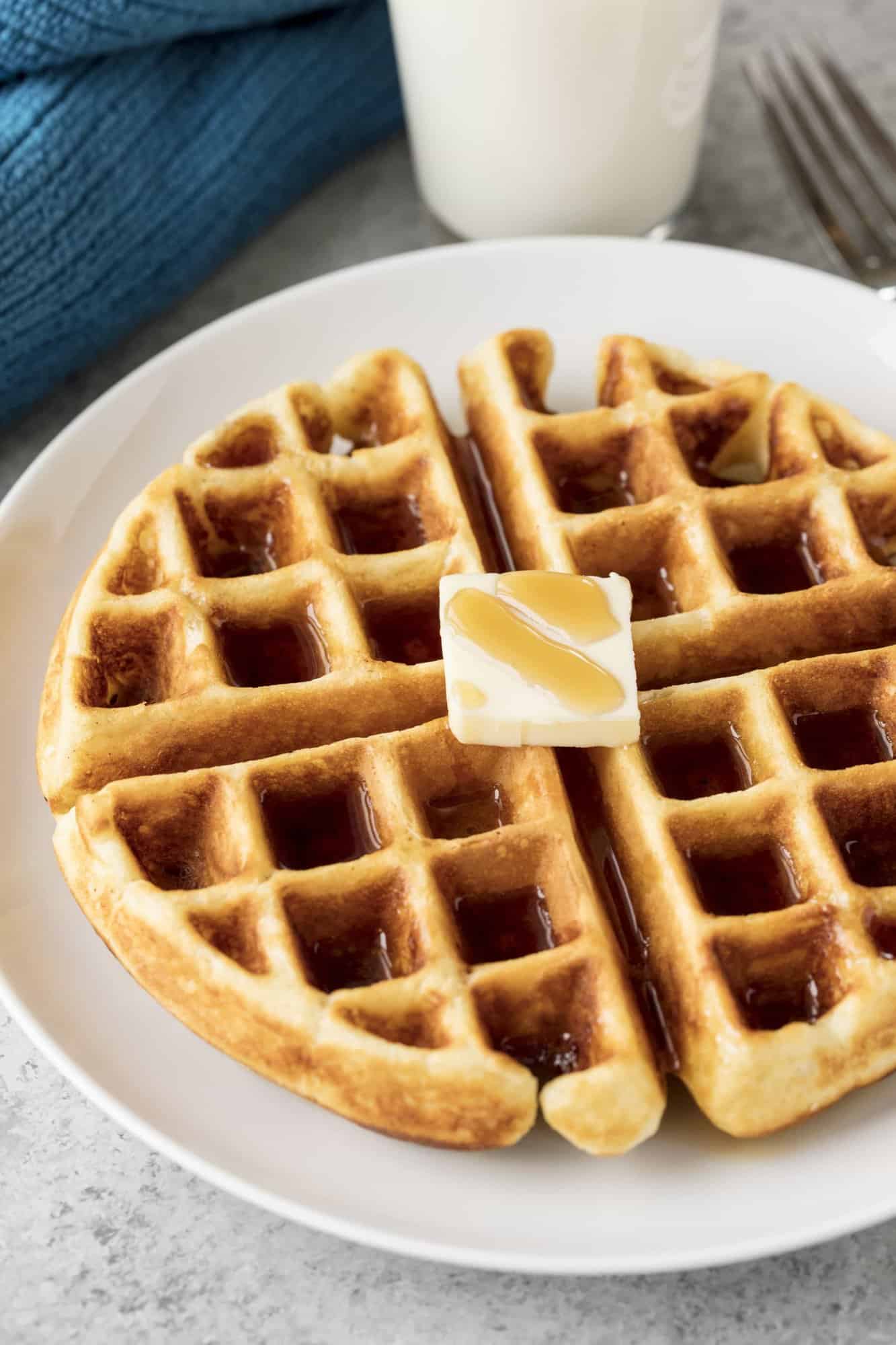 Greek Yogurt Waffle topped with syrup and a pad of butter on a white plate. 
