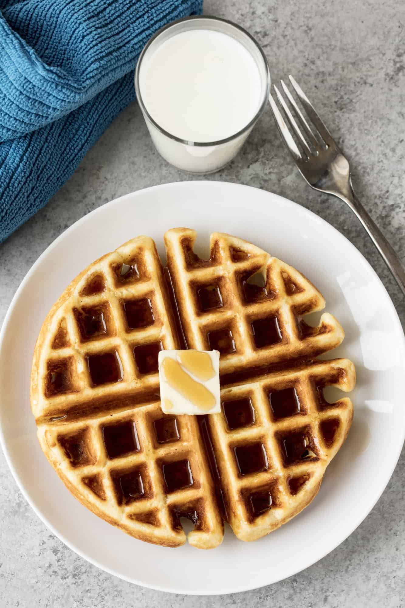 Birds eye view of a Greek Yogurt Waffle topped with syrup and a pad of butter on a white plate. 