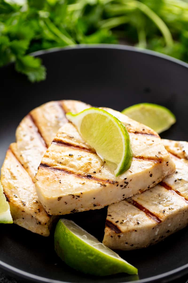 Grilled Swordfish fish on a black plate topped with a lime wedge.