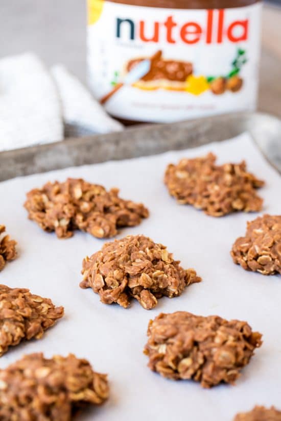 Closeup of Peanut Butter Nutella No Bake Cookies lined up on a baking sheet with a jar of nutella in the background