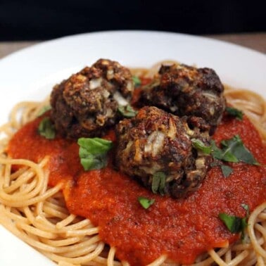 Spaghetti on a white plate topped with tomato sauce and meatballs.