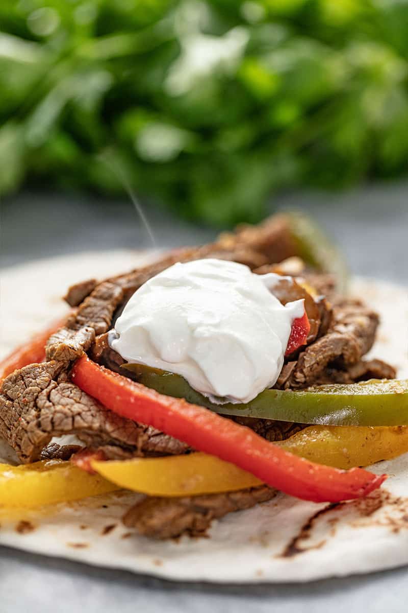 Steak Fajita topped with sour cream on a tortilla.