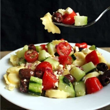 Greek Tortellini Salad on a white plate with a fork full of it.