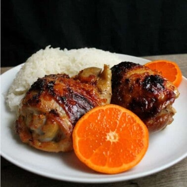 Orange Glazed Chicken Thigh on a white plate with a scoop of rice and half an orange.