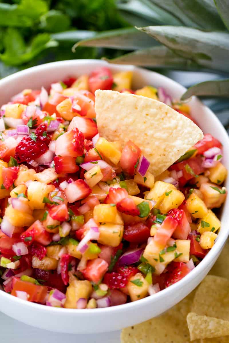 A tortilla chip dips into a bowl of Strawberry Pineapple Salsa