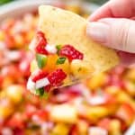 A tortilla chip with Strawberry Pineapple Salsa with pieces of pineapple, strawberry, onion, jalapeno