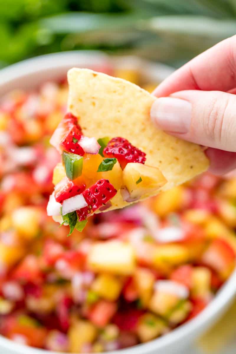 A tortilla chip with Strawberry Pineapple Salsa with pieces of pineapple, strawberry, onion, jalapeno