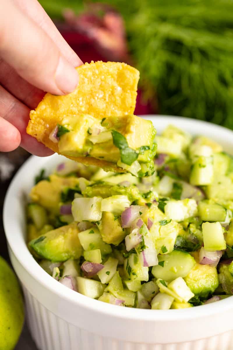 Chip dipping into some Avocado Fennel Salsa in a white bowl.