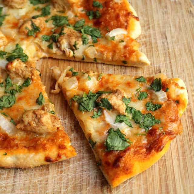 A slice of chicken tikka masala pizza that has been cut out from the whole pie on a wooden cutting board.