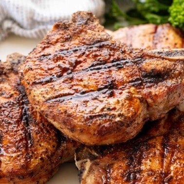 Stack of grilled pork chops on a white plate.