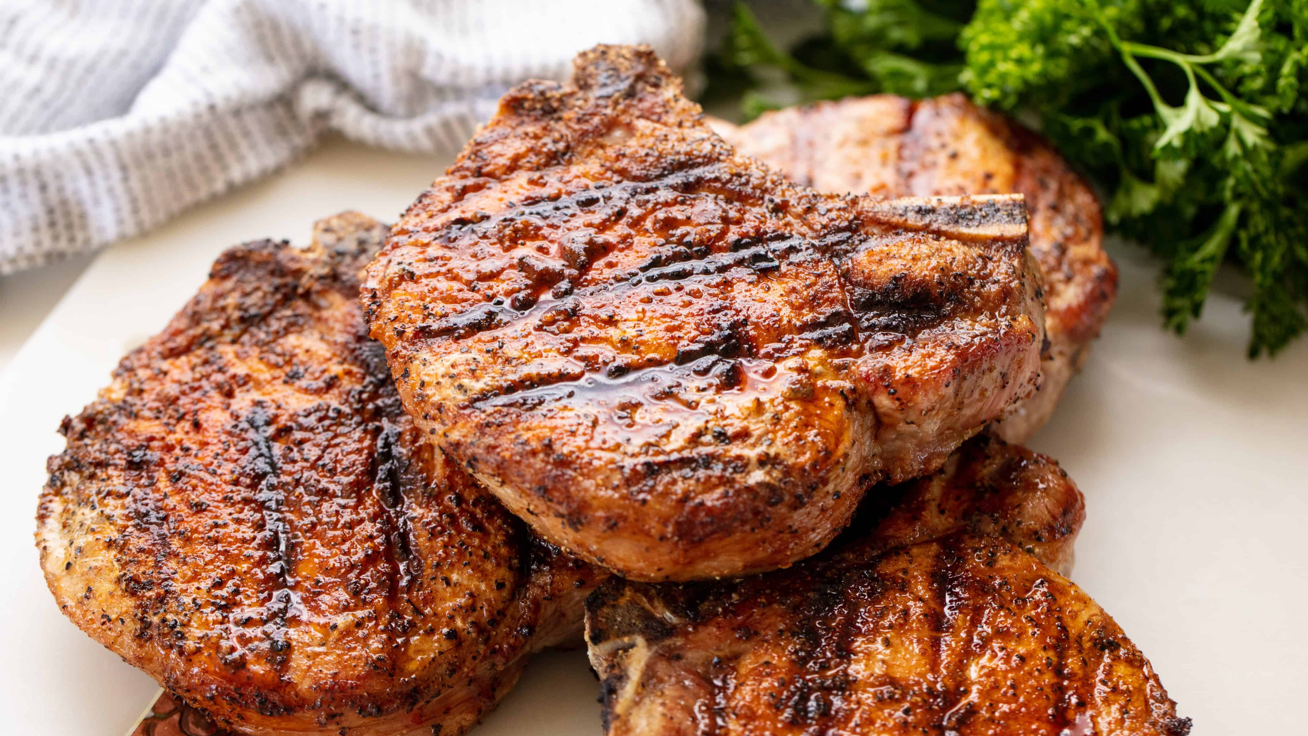 Stack of grilled pork chops on a white plate.