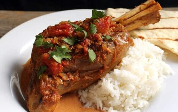 Tikka Masala Lamb Shank on a scoop of rice on a white plate.