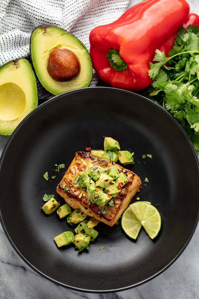 Avocado Salsa Sea Bass in a skillet with avocado salsa and slices of lime