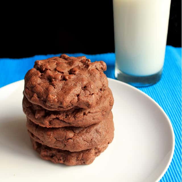 Freshly baked Best Ever Chocolate Cookies stacked on a plate, served with a cold glass of milk