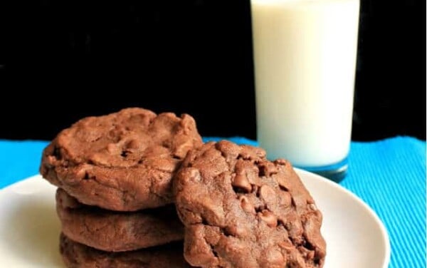 A stack of Chocolate Cookies on a white plate by a glass of milk
