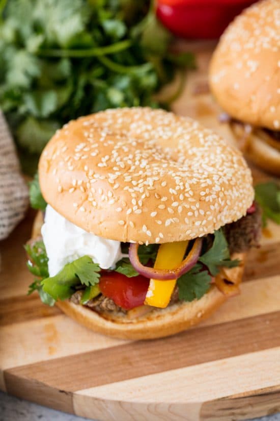 Fajita Burgers with grilled steak, bell pepper, red onion, cilantro and sour cream on a Sesame Bun