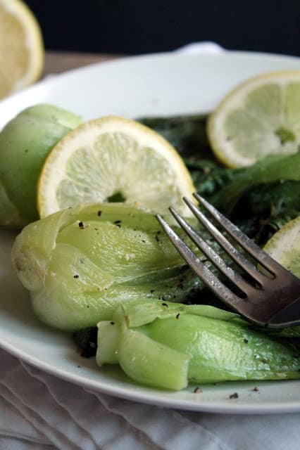 Lemon-Garlic Baby Bok Choy on a white plate with a fork on it.