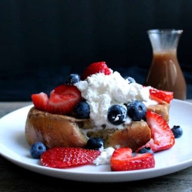 French toast on a white plate topped with whipped cream, blueberries, and strawberries.