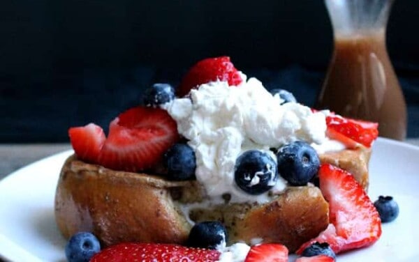 French toast on a white plate topped with whipped cream, blueberries, and strawberries.