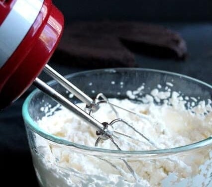 A bowl of whipping cream with a hand mixer in it.