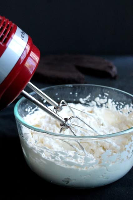 A bowl of whipping cream with a hand mixer in it.