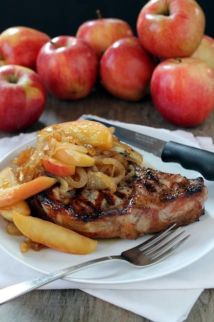 Apple Pork Chop topped with onions on a white plate.