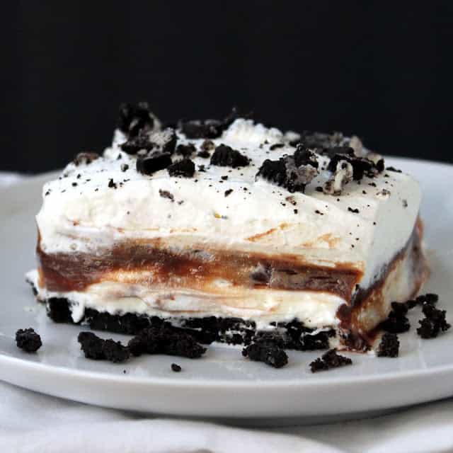 Close up of Cookies and Cream Layered Dessert topped with crushed Oreo cookies on a white plate.