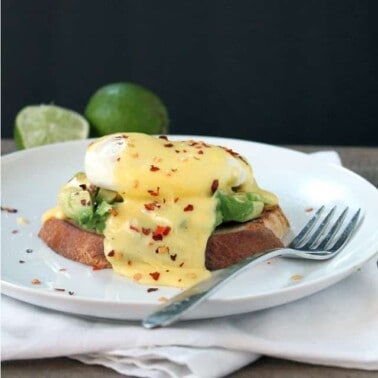 Eggs Benedict a la Avocado Toast on a white plate next to a fork.