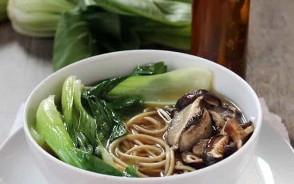 Ramen with mushrooms and green vegetables in it all in a white bowl.