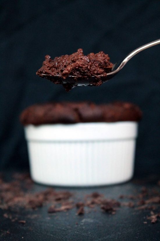 Spoon of chocolate souffle with the full ramekin of chocolate souffle in the background