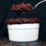 Spoon of chocolate souffle with the full ramekin of chocolate souffle in the background